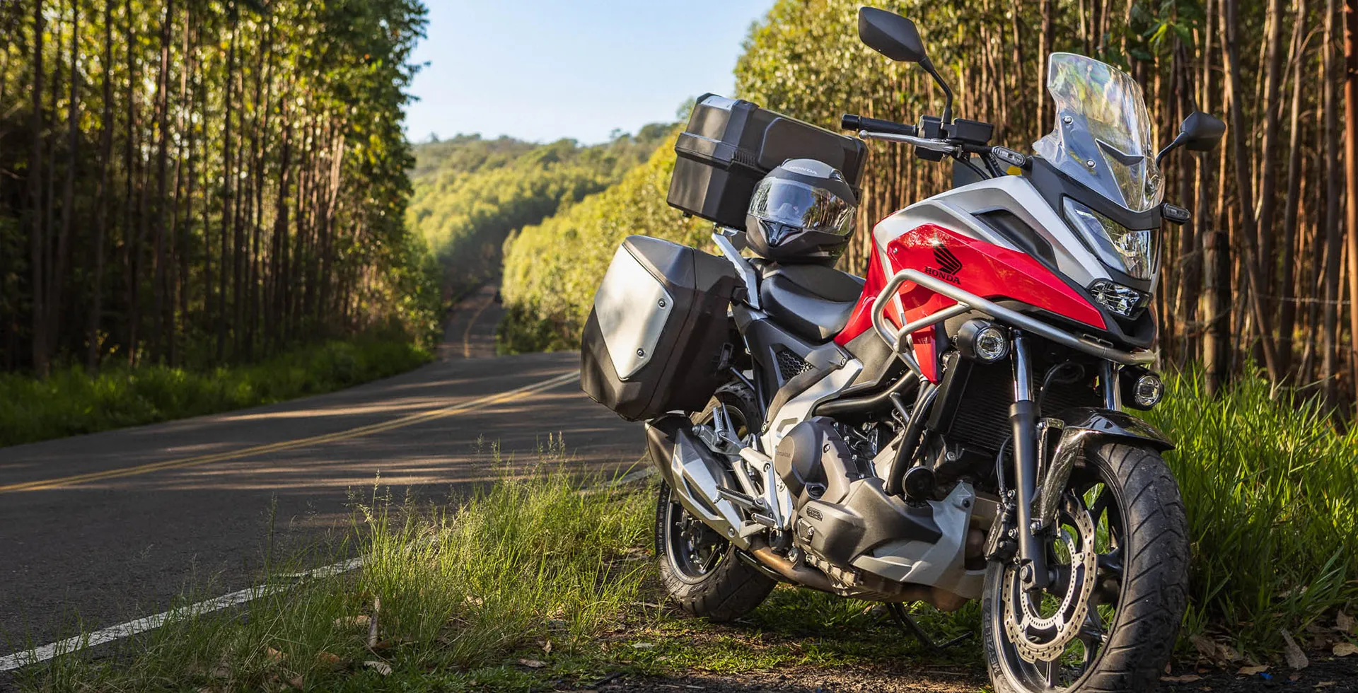 NC 750X vermelha estacionada em gramado ao lado da estrada